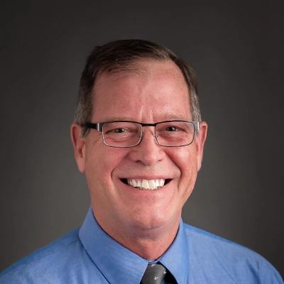 Chiropractor Mark McCann Smiling In Front Of Grey Background